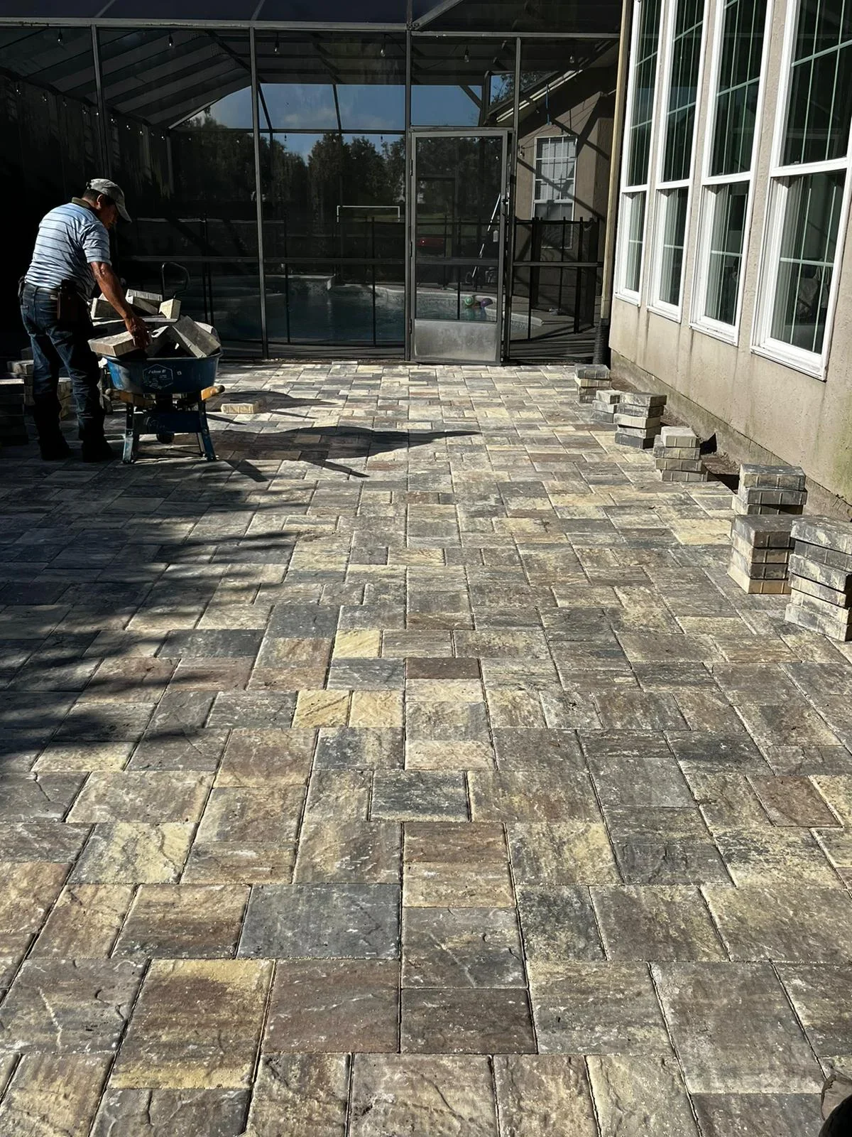 Worker installing tumbled stone pavers in running bond pattern on patio with screened enclosure