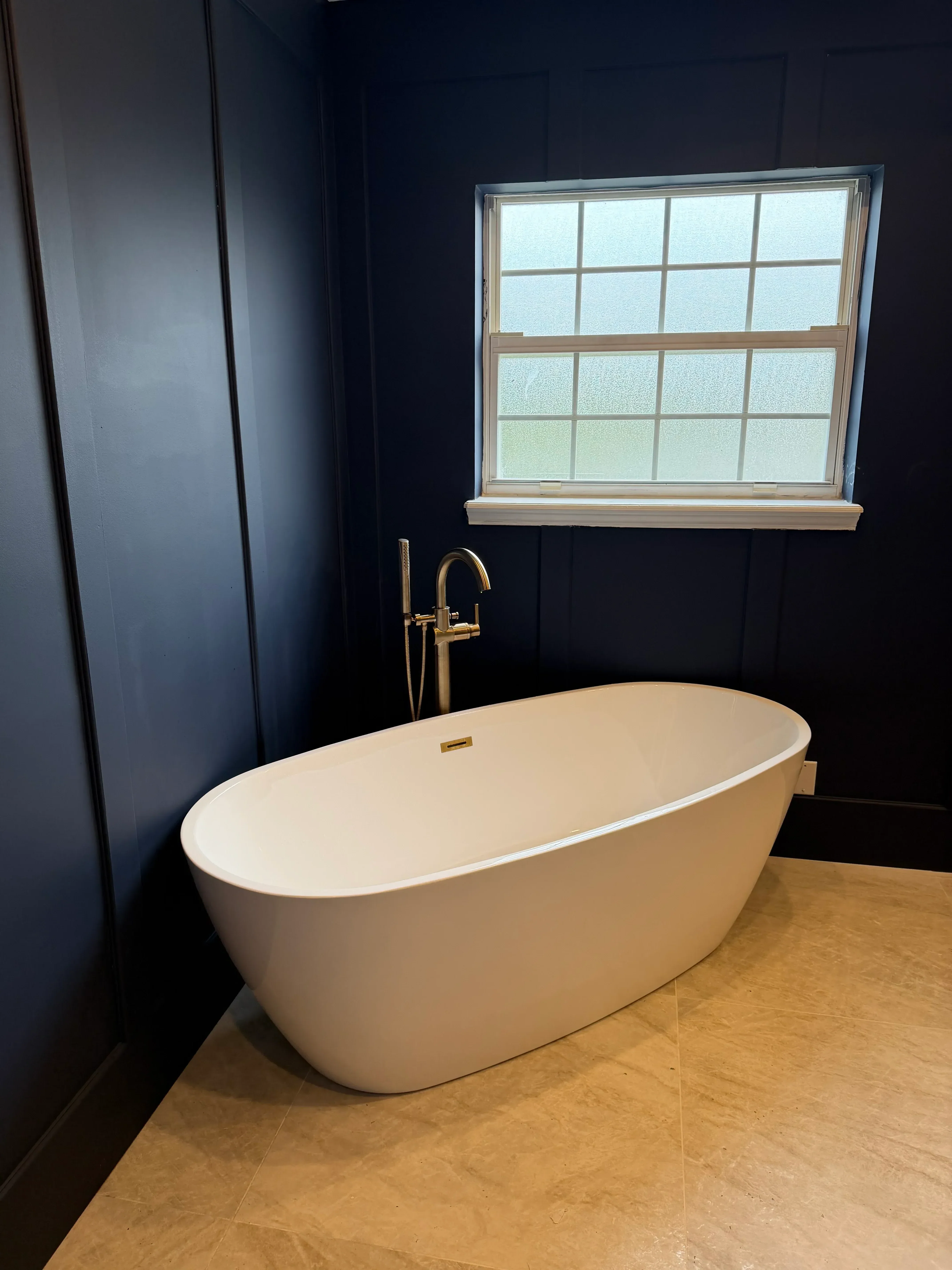 Round white vessel sink with brass faucet mounted on wood vanity cabinet next to installed double-hung window
